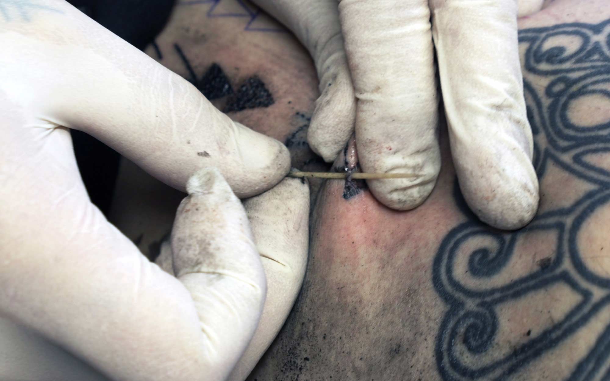 Subdermal Tattooing mit einer Nadel aus einem Vogelknochen, die in Farbe getränktes Garn hinter sich durch die Haut zieht. / Quelle: exarc.net/ark:/88735/10654 / Foto: Candice Nel
